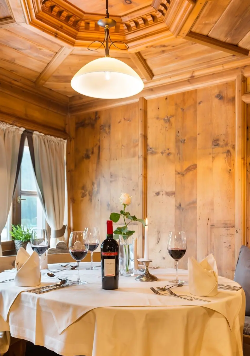 Gemütlich gedeckter Tisch mit Rotwein und Kerzenlicht im traditionellen Restaurant des Sporthotel Cristall.