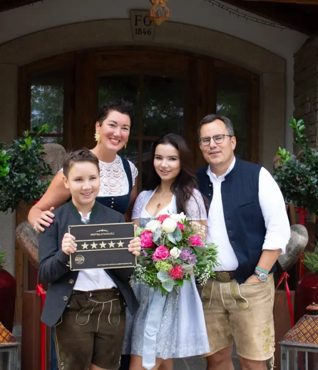 Die Familie des Ortner's Resort präsentiert stolz die 5-Sterne-Auszeichnung vor dem traditionellen Hoteleingang.