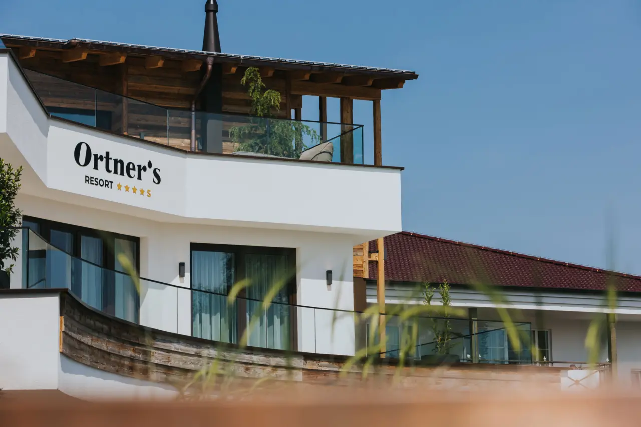 Moderne Fassade des Ortner's Resort mit Logo, Holz- und Glaselementen unter blauem Himmel.