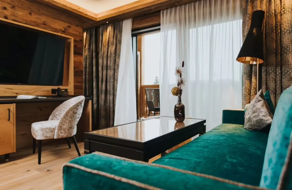 Modernes Hotelzimmer im Ortner's Resort mit tealfarbenem Sofa, Holzelementen und Zugang zum Balkon.