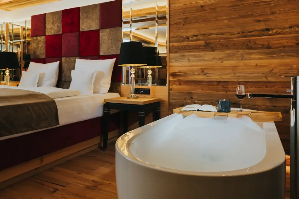 Luxuriöses Hotelzimmer im Ortner's Resort mit freistehender Badewanne, Schaumbad, Rotwein und Holzakzenten für entspannte Momente.