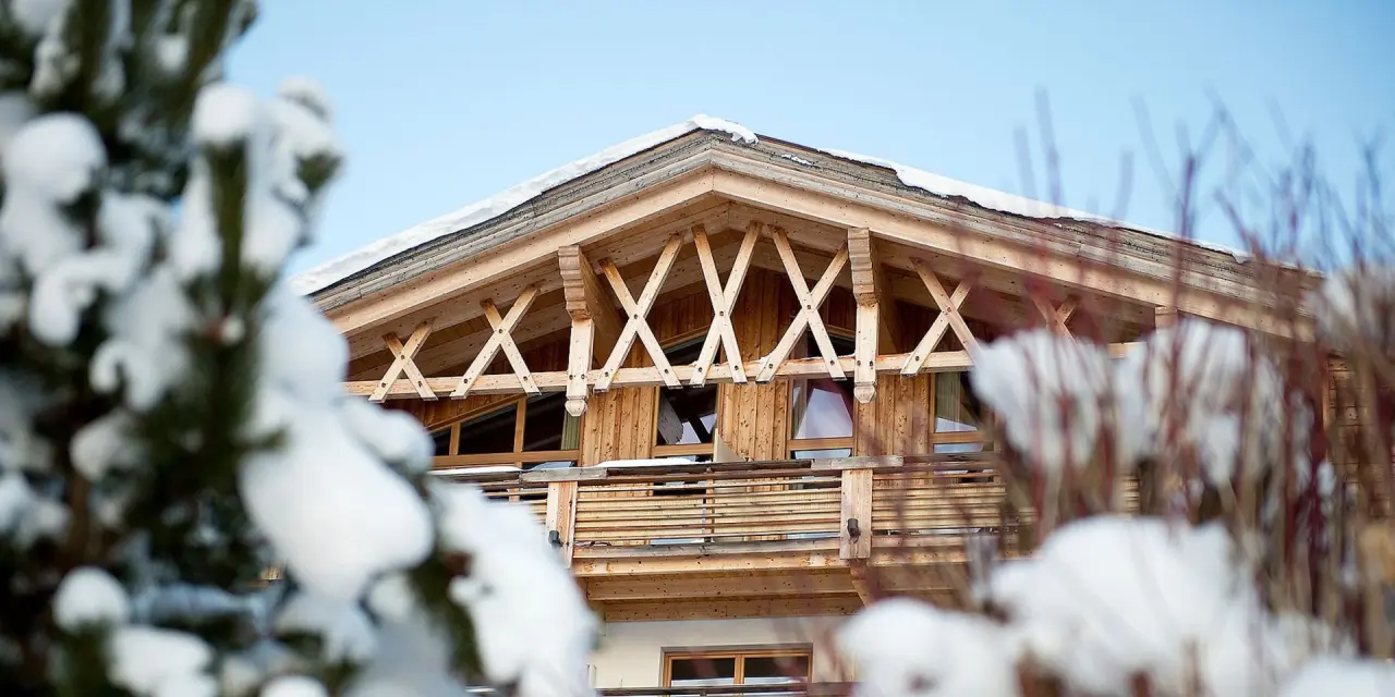 Detailansicht der verschneiten Holzfassade mit Balkon und Giebel des Inntalerhof - DAS Panoramahotel im Winter.