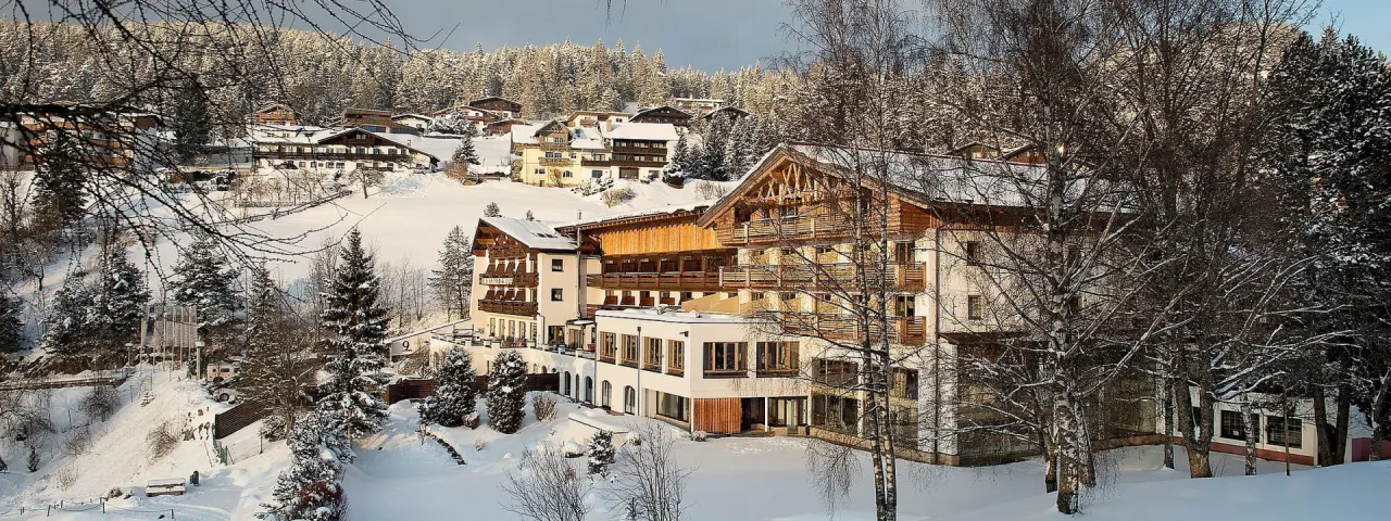 Winterliche Aussenansicht des Inntalerhof - DAS Panoramahotel, umgeben von verschneiten Bäumen und Häusern in den Bergen.