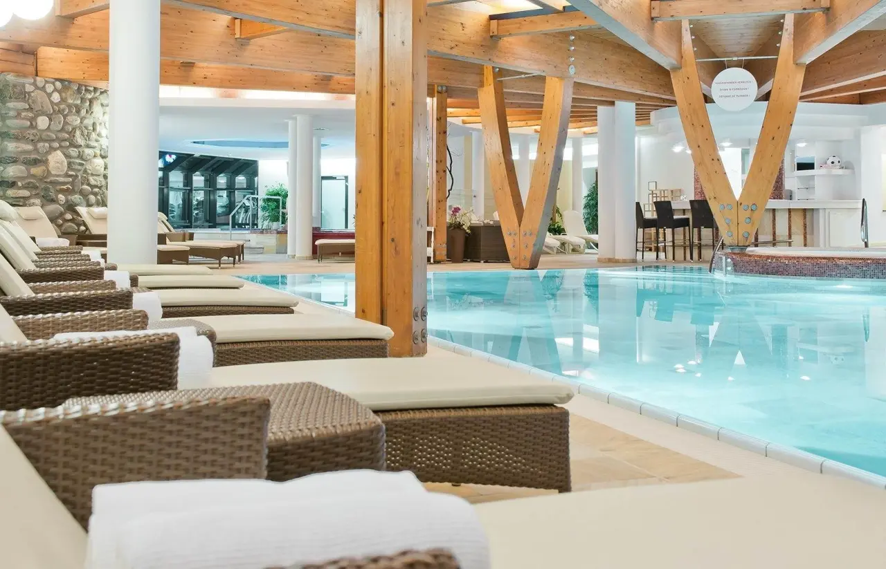 Grosszügiger Innenpoolbereich mit Holzarchitektur, Steinwand und bequemen Liegen im Hotel Alpina Deluxe.