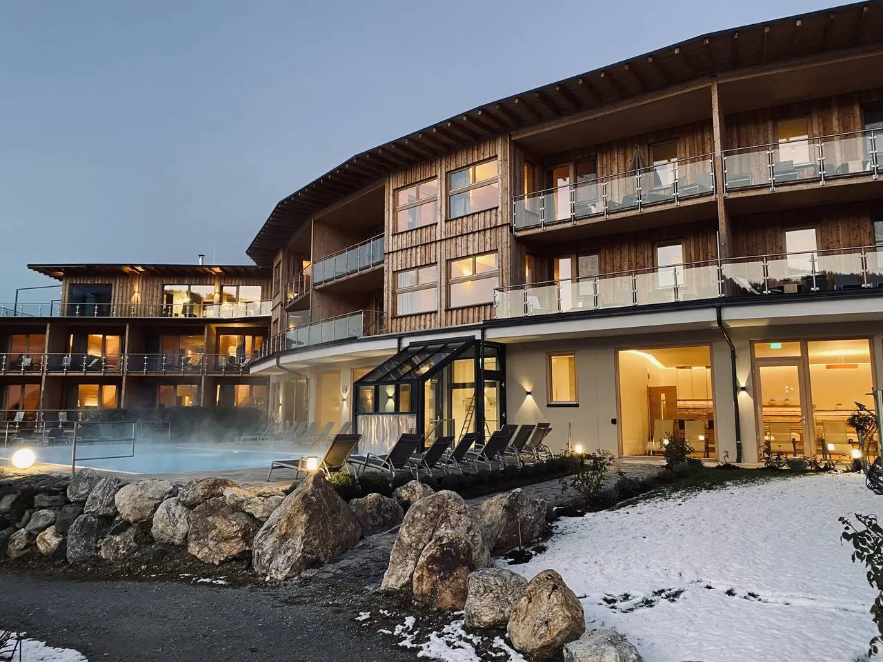 Aussenansicht des Hotel Molzbachhof bei Dämmerung mit dampfendem Aussenpool und verschneiter Landschaft.