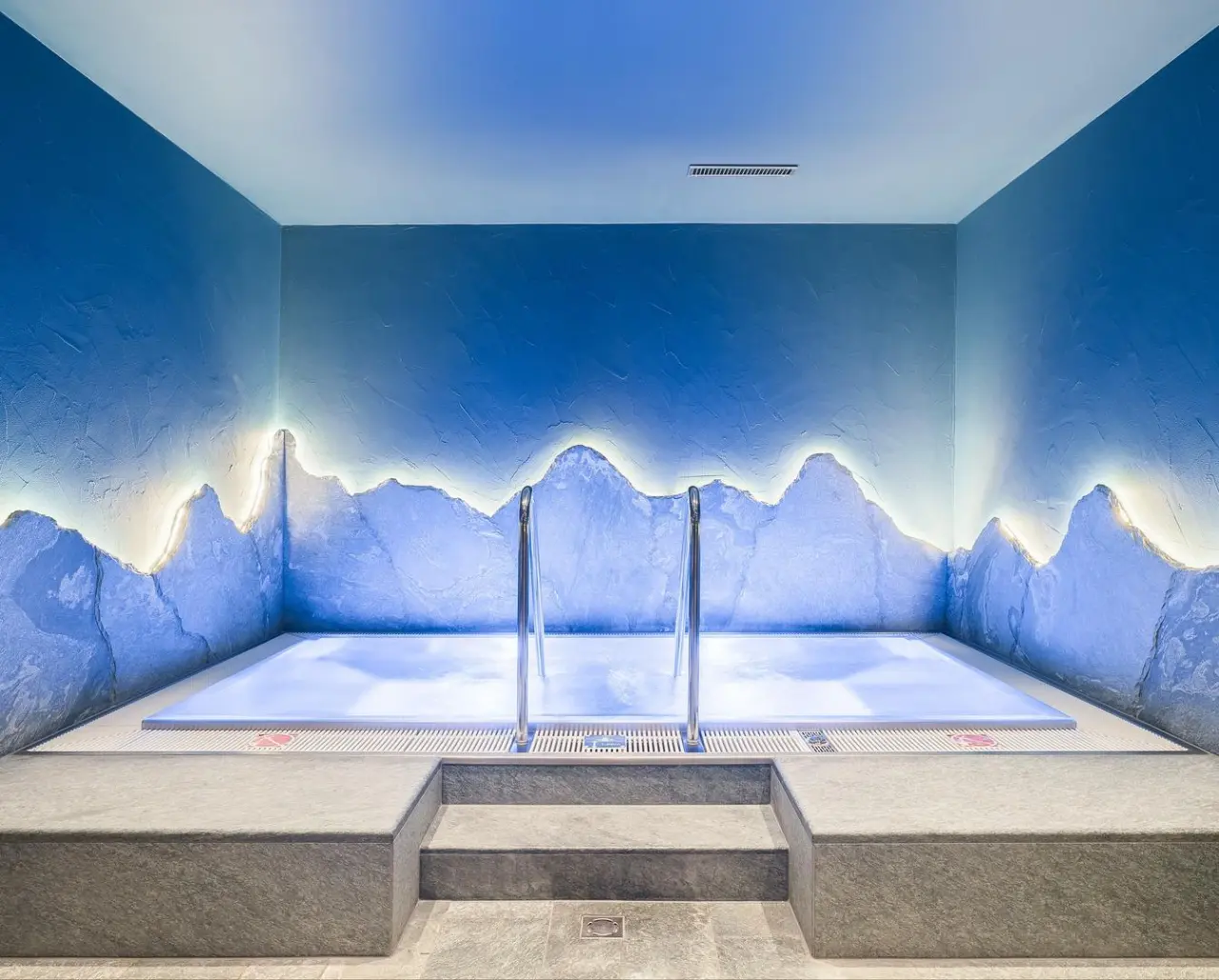 Blau beleuchteter Whirlpool mit einzigartigem Bergwand-Design im Spa des Riffelalp Resort 2222 m.