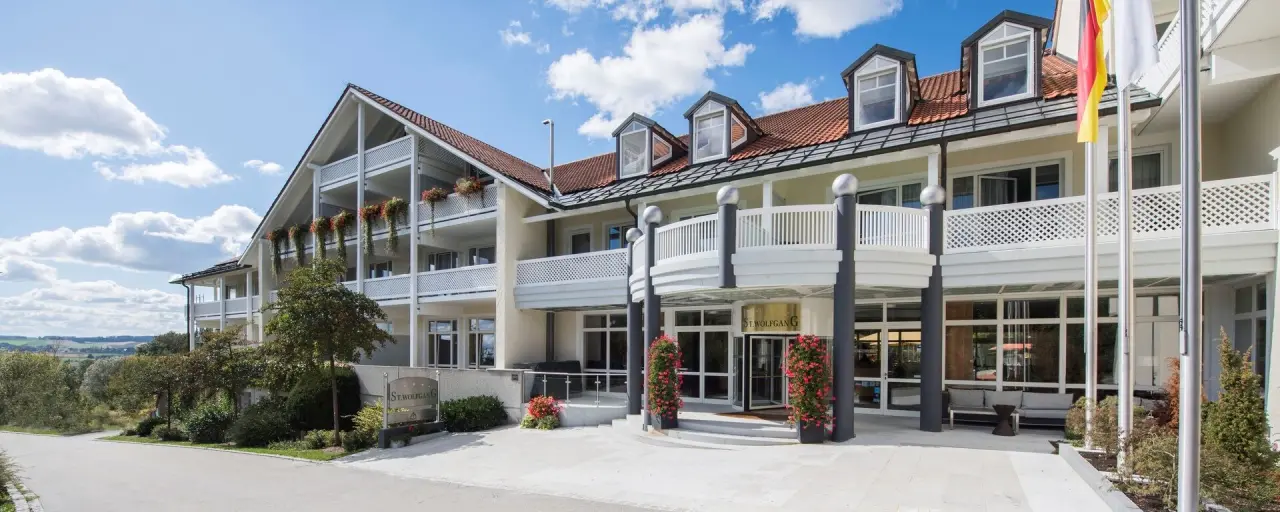 Elegante Aussenansicht des Hotel St. Wolfgang***** mit blühenden Balkonen und einladendem Eingangsbereich an einem sonnigen Tag.