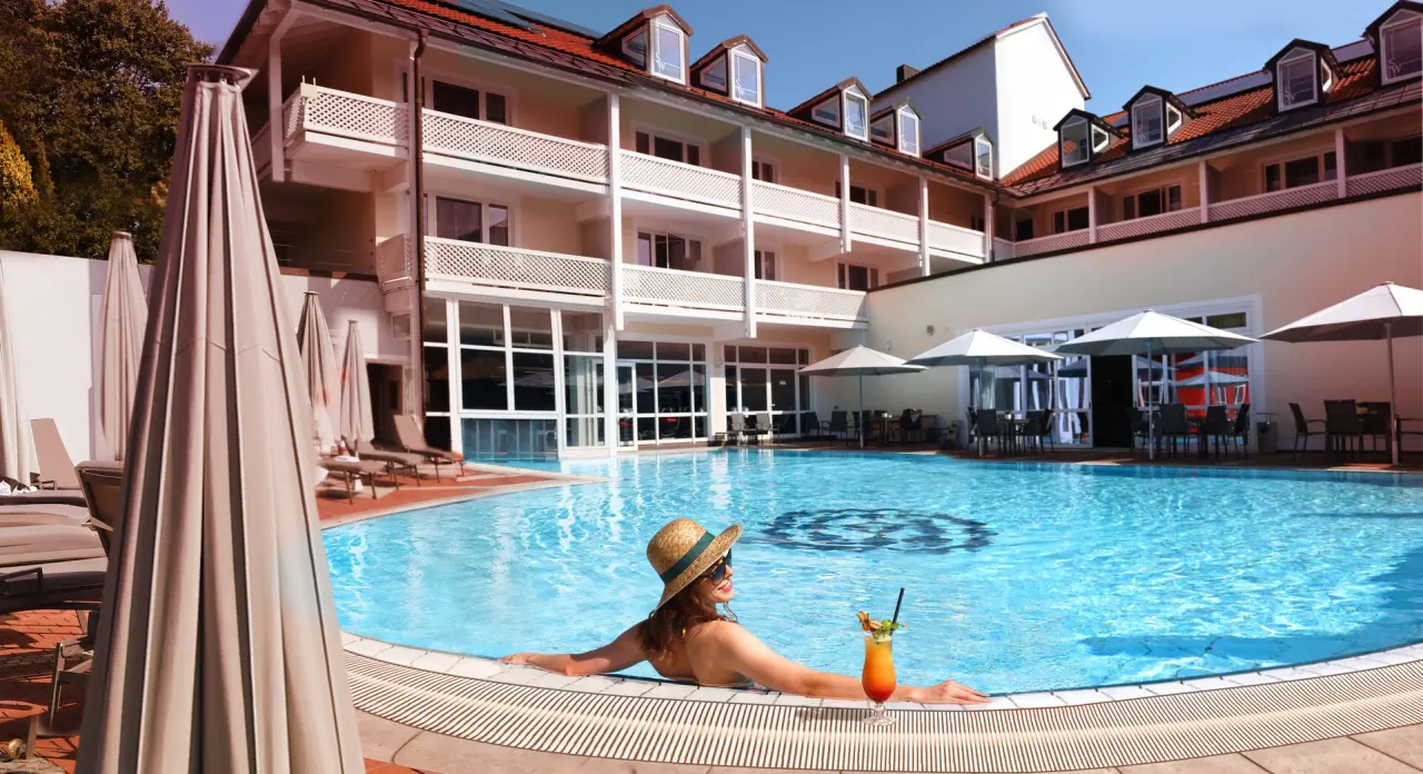 Entspannte Frau mit Cocktail im Aussenpool des Hotel St. Wolfgang***** mit Blick auf die Hotelanlage.