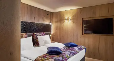 Modernes Hotelzimmer im Sporthotel Ellmau mit Holzwänden, Doppelbett und Flachbildfernseher für entspannte Nächte.