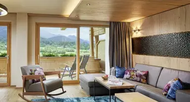Geräumiges Hotelzimmer im Sporthotel Ellmau mit gemütlicher Sitzecke, Balkon und Panoramablick auf die Tiroler Berge.