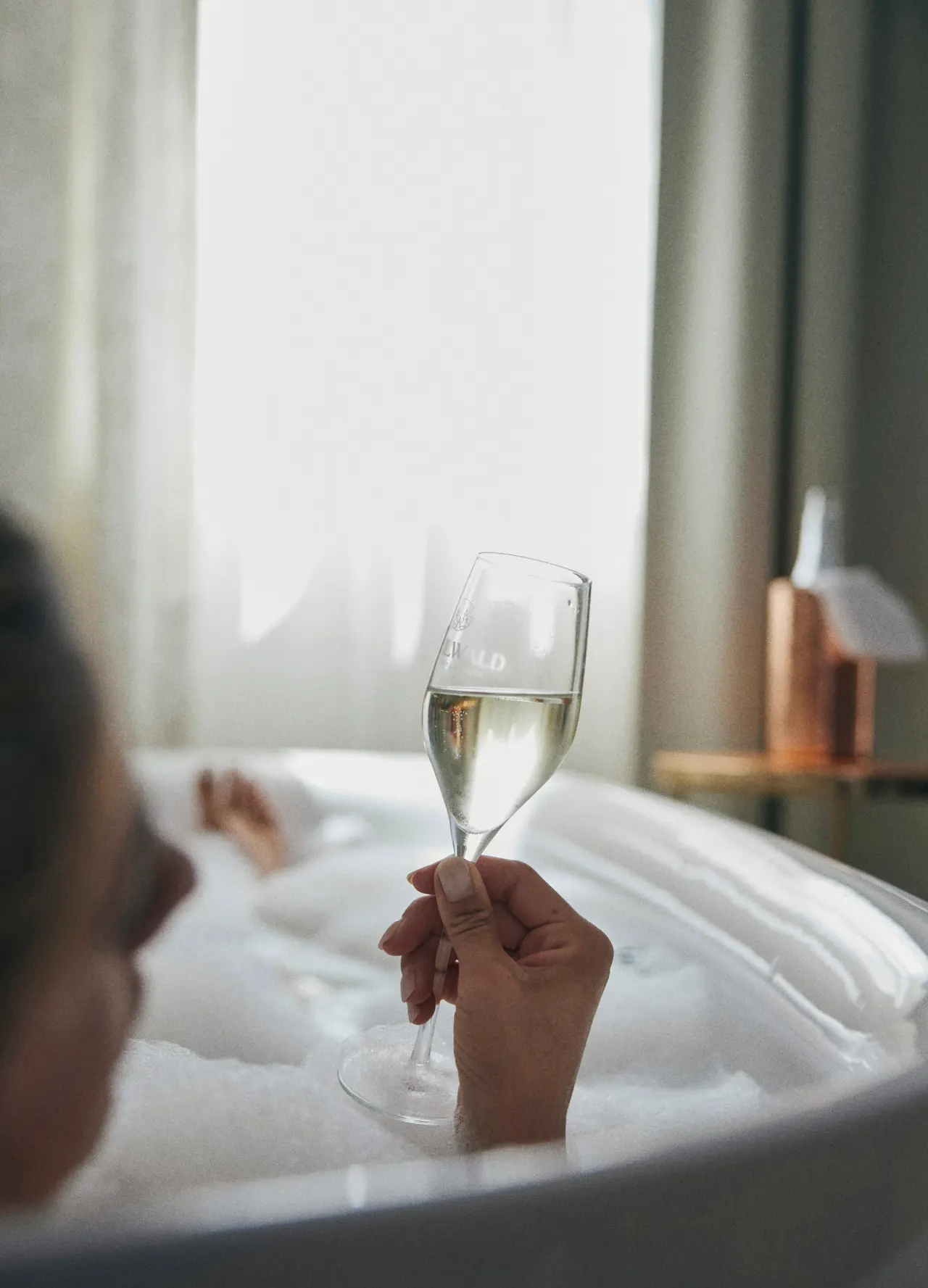 Gast genießt ein entspannendes Schaumbad mit einem Glas Sekt im stilvollen Badezimmer des Hotel Guglwald.