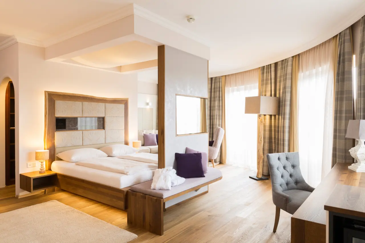 Helle, komfortable Suite im Hotel Guglwald mit Doppelbett, elegantem Sitzbereich und Holzboden für entspannte Aufenthalte.