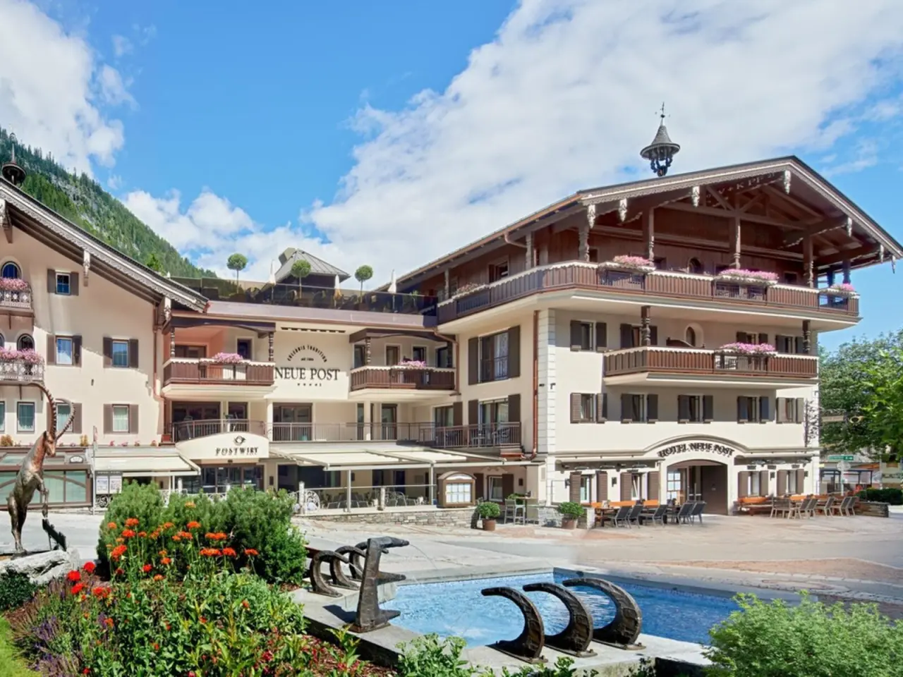 Traditionelles Hotel Neue Post in den Alpen mit blühenden Blumen und Brunnen vor Bergkulisse