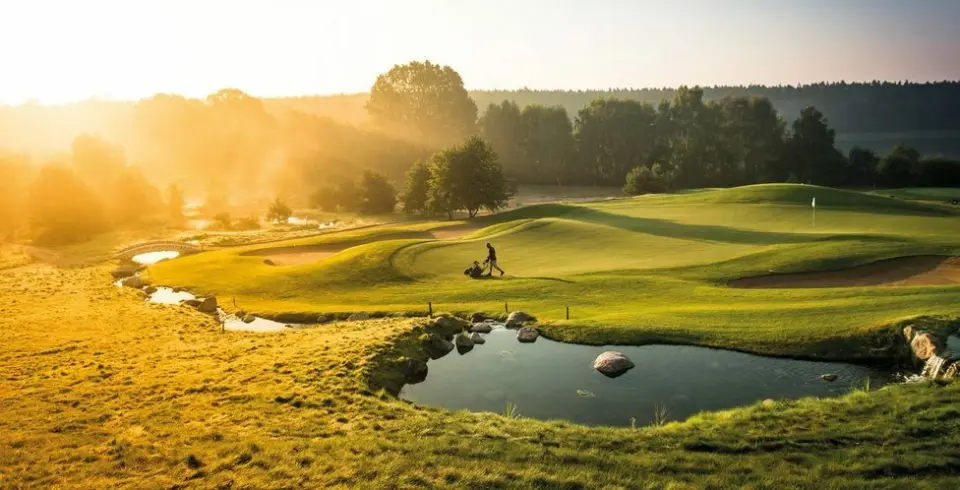 Sonnenaufgang über dem malerischen Golfplatz von Schloss Basthorst mit Golfer und Wasserhindernis.