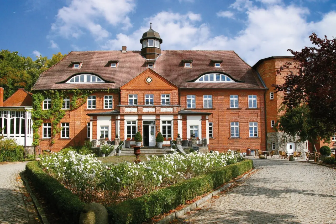 Majestätisches Schloss Basthorst mit roter Backsteinfassade und gepflegtem Vorgarten unter blauem Himmel.