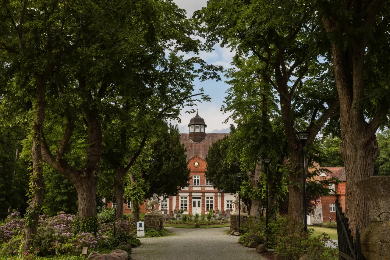 Majestätischer Eingang von Schloss Basthorst mit historischem Gebäude, umrahmt von alten Bäumen und grüner Parkanlage.