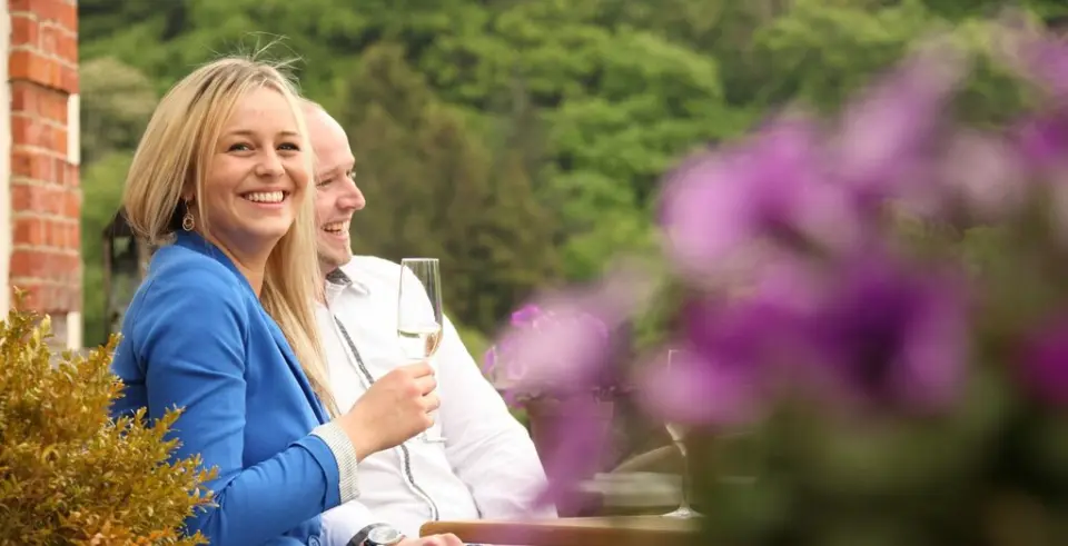 Lachende Gäste genießen entspannte Momente mit Getränken im grünen Gartenbereich von Schloss Basthorst.