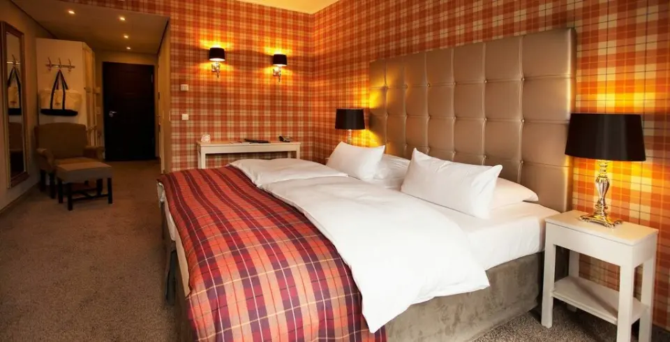 Gemütliches Hotelzimmer im Schloss Basthorst mit karierter Tapete, Doppelbett und warmem Licht.