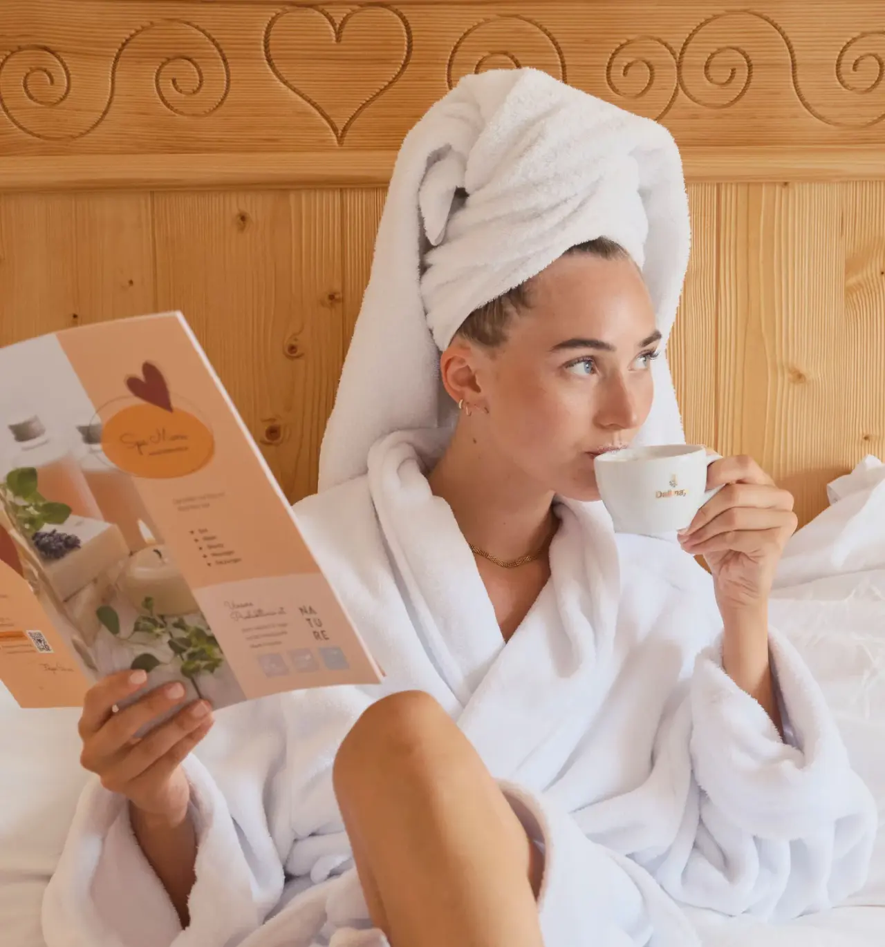 Frau im Bademantel entspannt mit Spa-Magazin und Kaffee im Bett des Genuss und Vitalhotel Moisl.