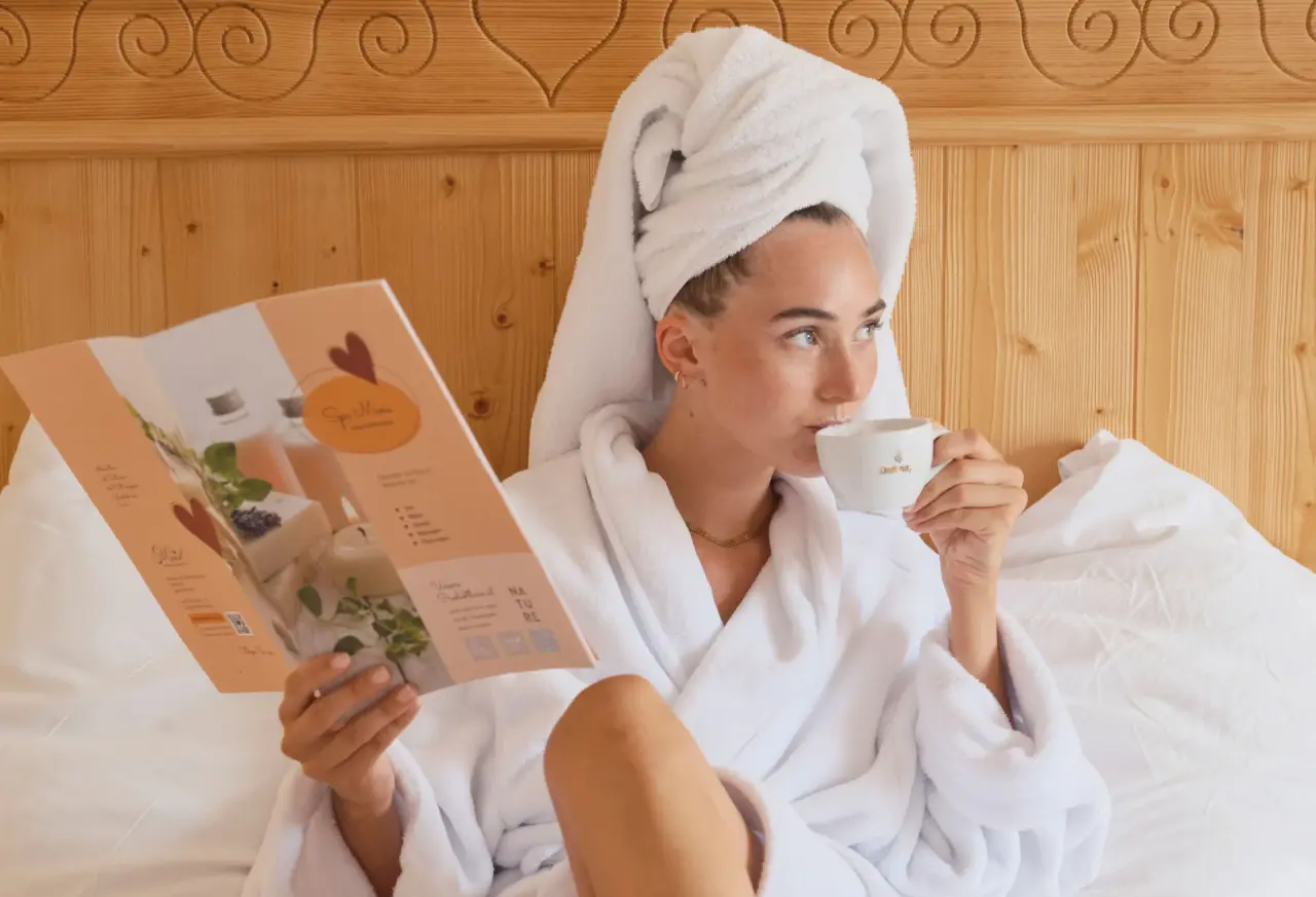 Frau im Bademantel mit Handtuch auf dem Kopf liest ein Spa-Magazin im Bett des Genuss und Vitalhotel Moisl.