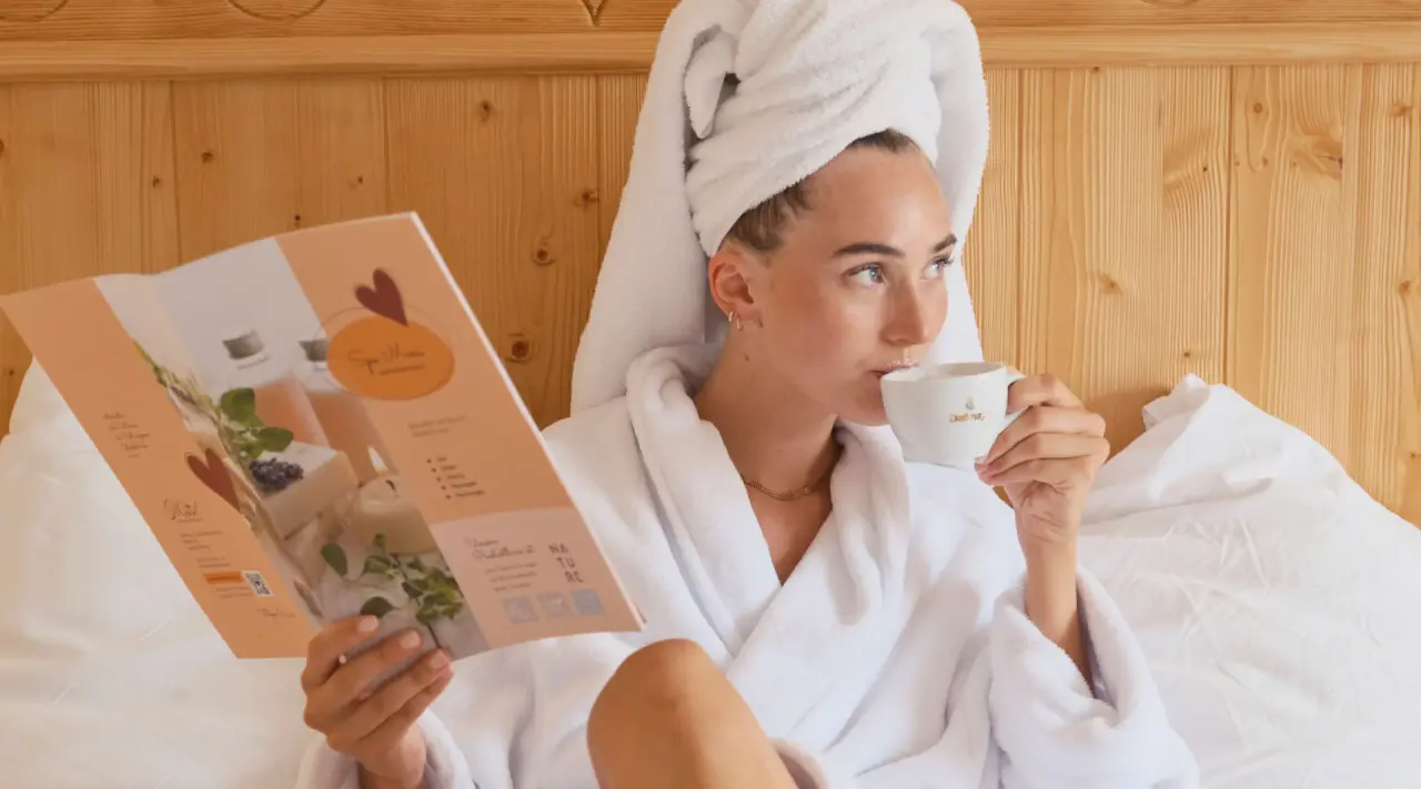 Entspannte Frau im Bademantel liest das Spa-Menü im Zimmer des Genuss und Vitalhotel Moisl.