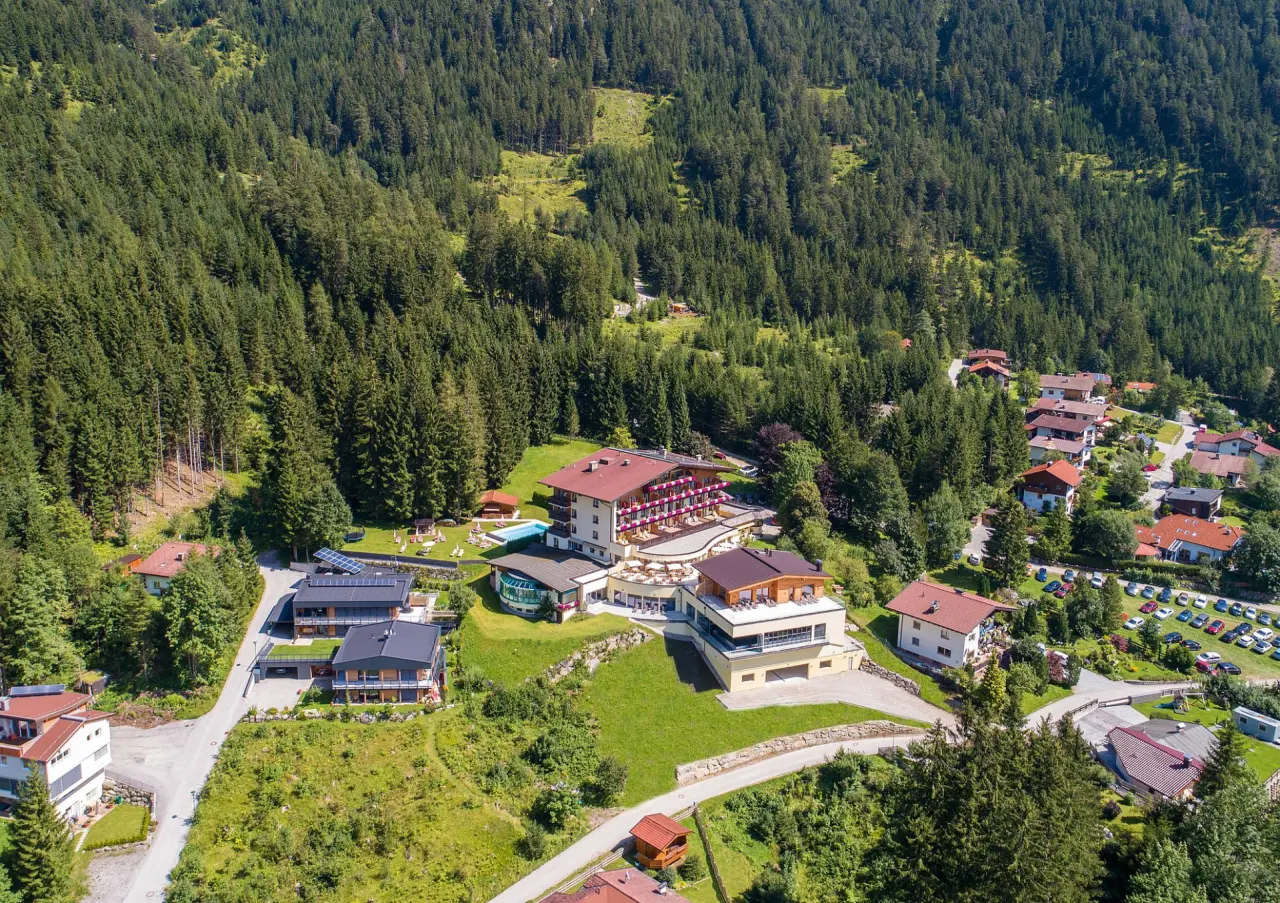 Luftaufnahme des Naturhotel Alpenblick in den Bergen, umgeben von dichtem Wald, mit Hotelkomplex und Aussenpool.