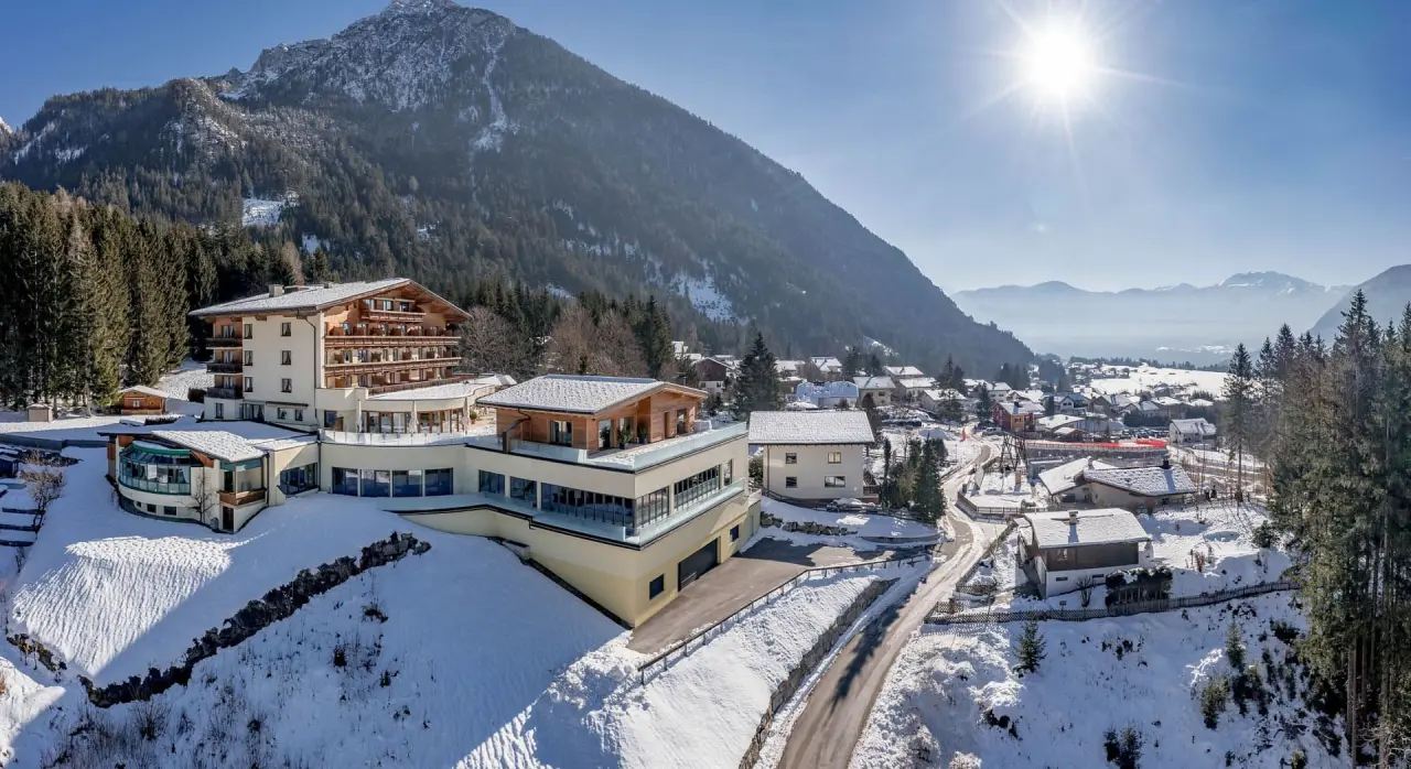 Winterliche Aussenansicht des Naturhotel Alpenblick mit schneebedeckten Bergen und strahlendem Sonnenschein.