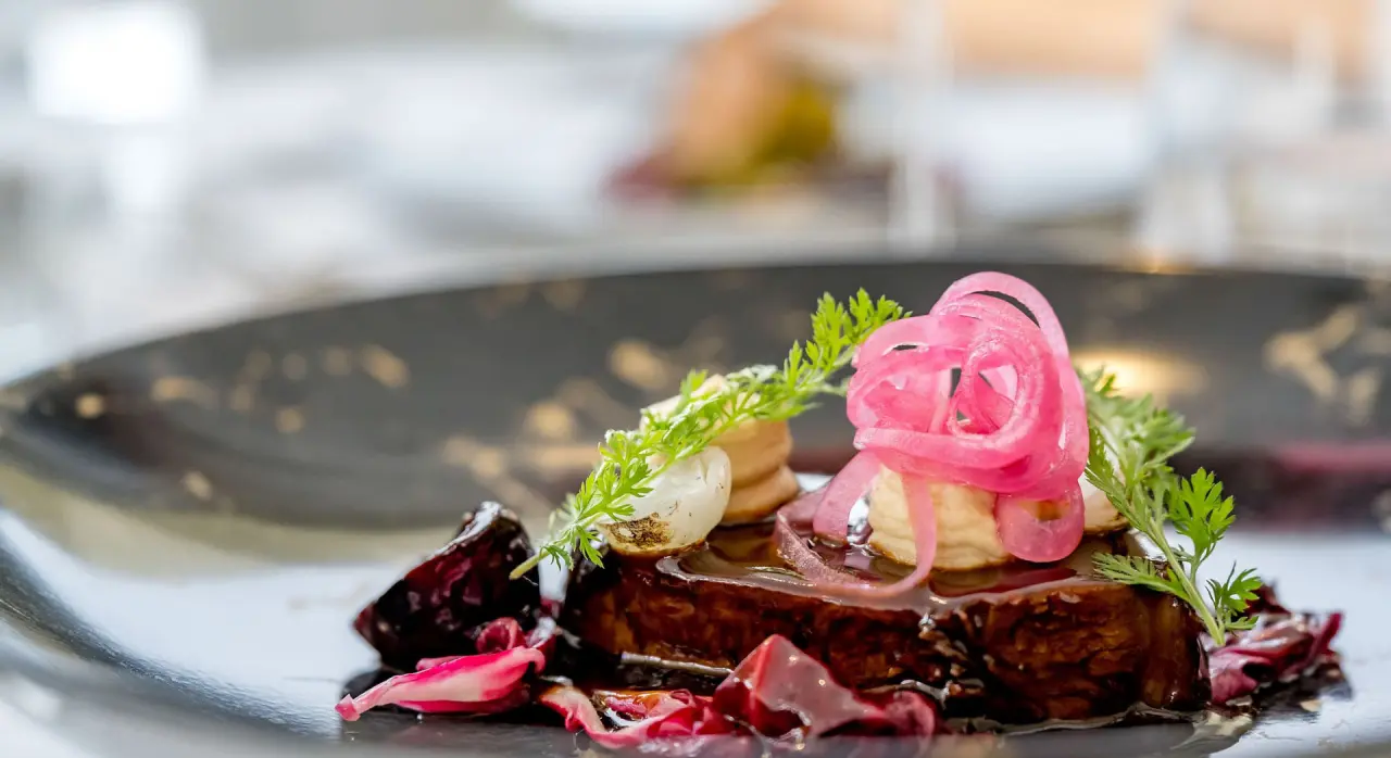 Fein angerichtetes Gericht mit rosa Zwiebeln und Kräutern im Restaurant des Naturhotel Alpenblick.
