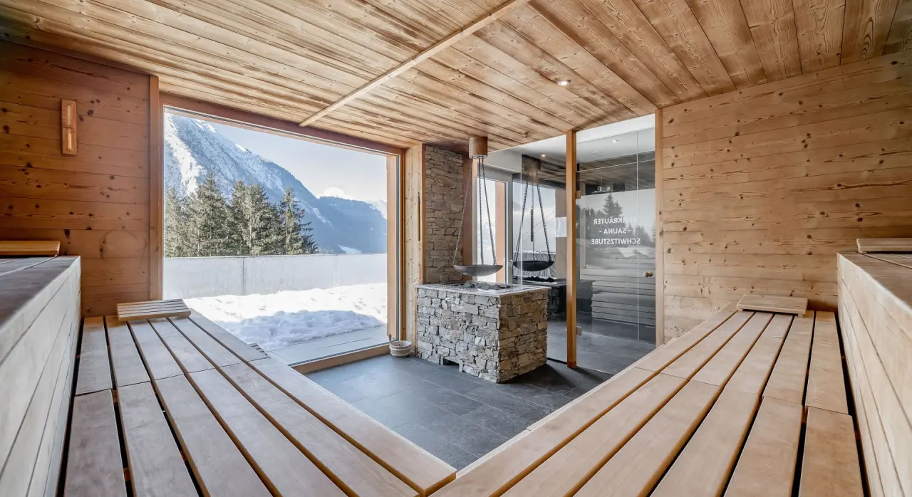 Panoramasauna mit Bergblick im Naturhotel Alpenblick. Entspannung in der Kräutersauna mit verschneiter Berglandschaft.