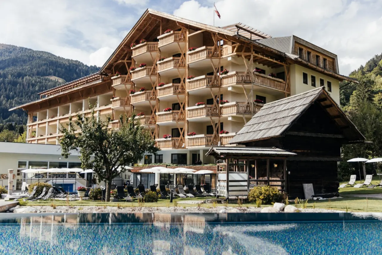 Aussenansicht des traditionellen Hotel Pulverer mit Aussenpool und Liegewiese vor alpiner Bergkulisse.