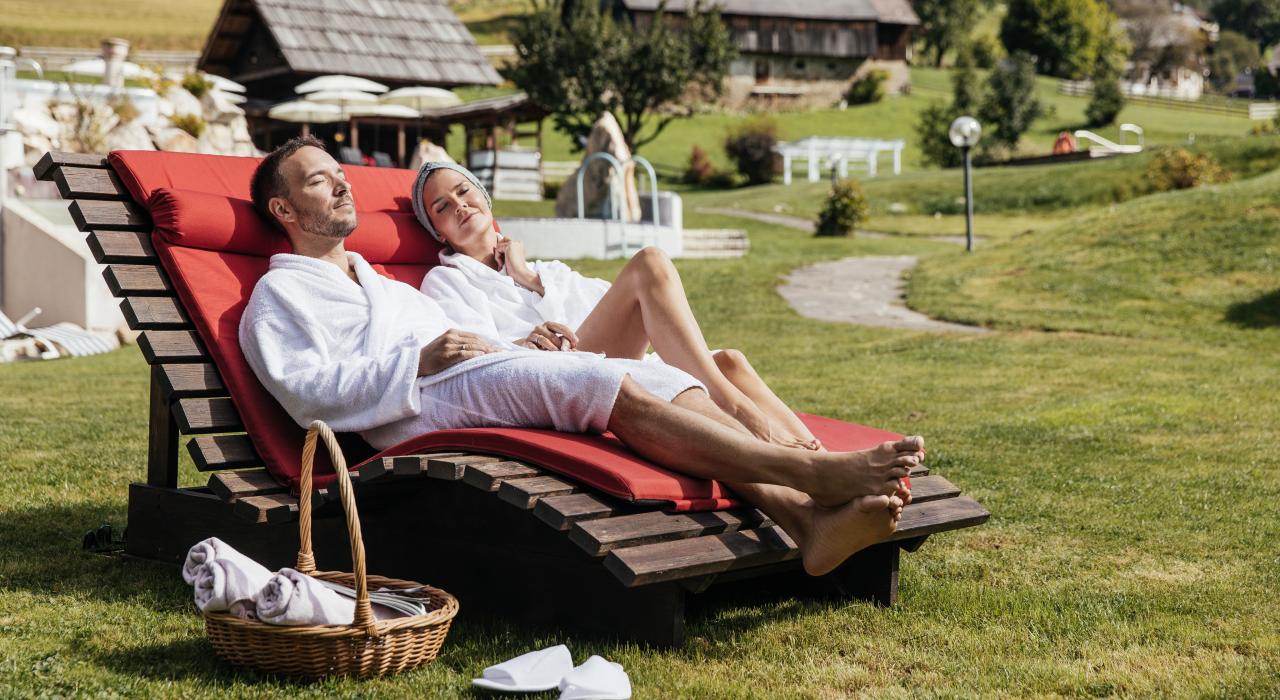 Hotel Pulverer in Bad Kleinkirchheim – Paar entspannt auf Sonnenliegen im grünen Hotelgarten | Wellnesshotel Kärnten