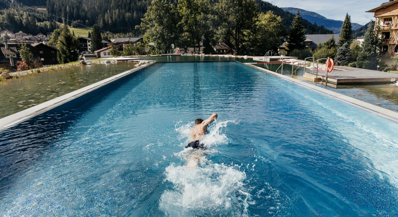 Hotel Pulverer in Bad Kleinkirchheim – Außenpool mit Schwimmer und Bergkulisse | Wellnesshotel Kärnten