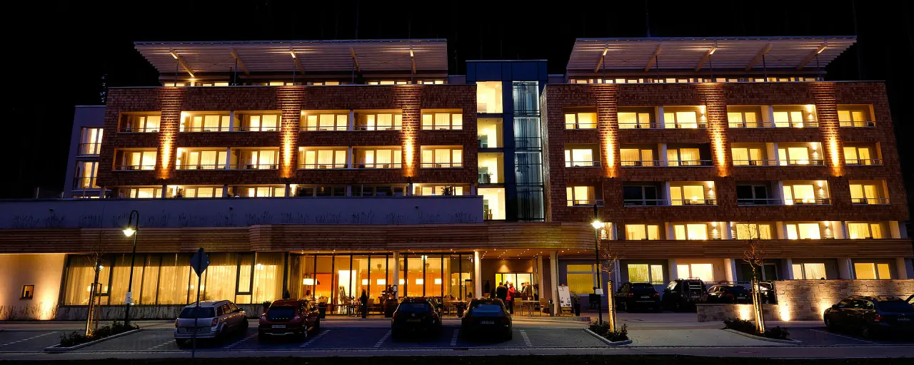 Hotel Bären Titisee bei Nacht mit beleuchteter Holzfassade und warmen Lichtern. Einladende Aussenansicht des modernen Wellnesshotels.