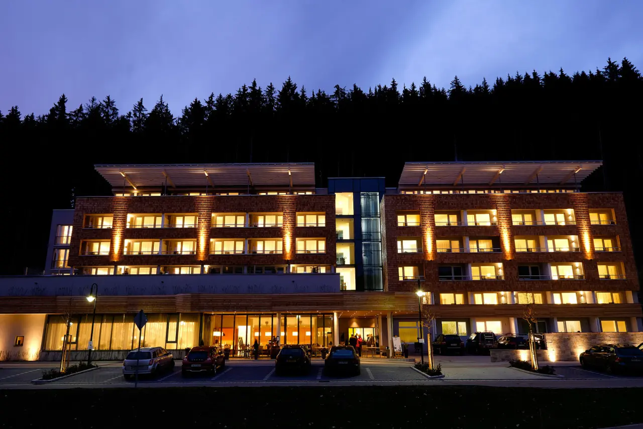 Modernes Hotel Bären Titisee bei Abenddämmerung mit beleuchteten Fenstern und Wald im Hintergrund.