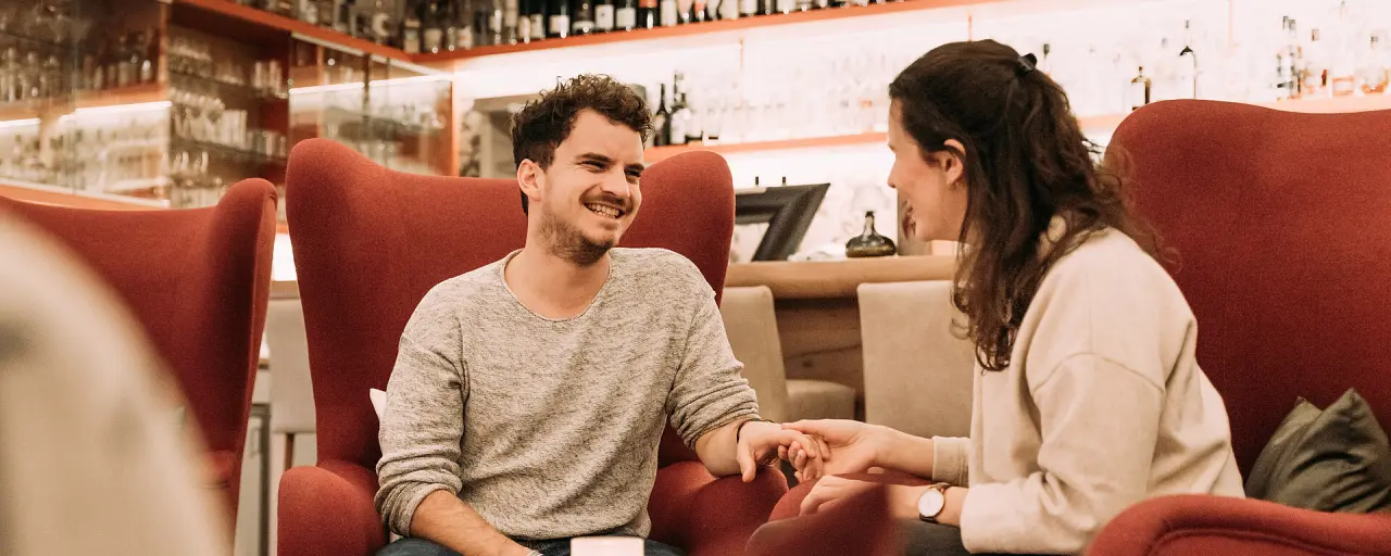 Zwei lachende Gäste in roten Sesseln an der Bar des Hotel Bären Titisee, genießen die entspannte Atmosphäre.