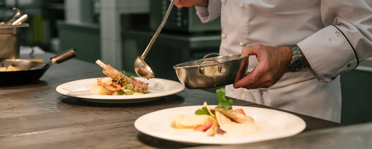 Koch beim Anrichten eines Gourmet-Hauptgerichts in der Küche des Hotel Bären Titisee.