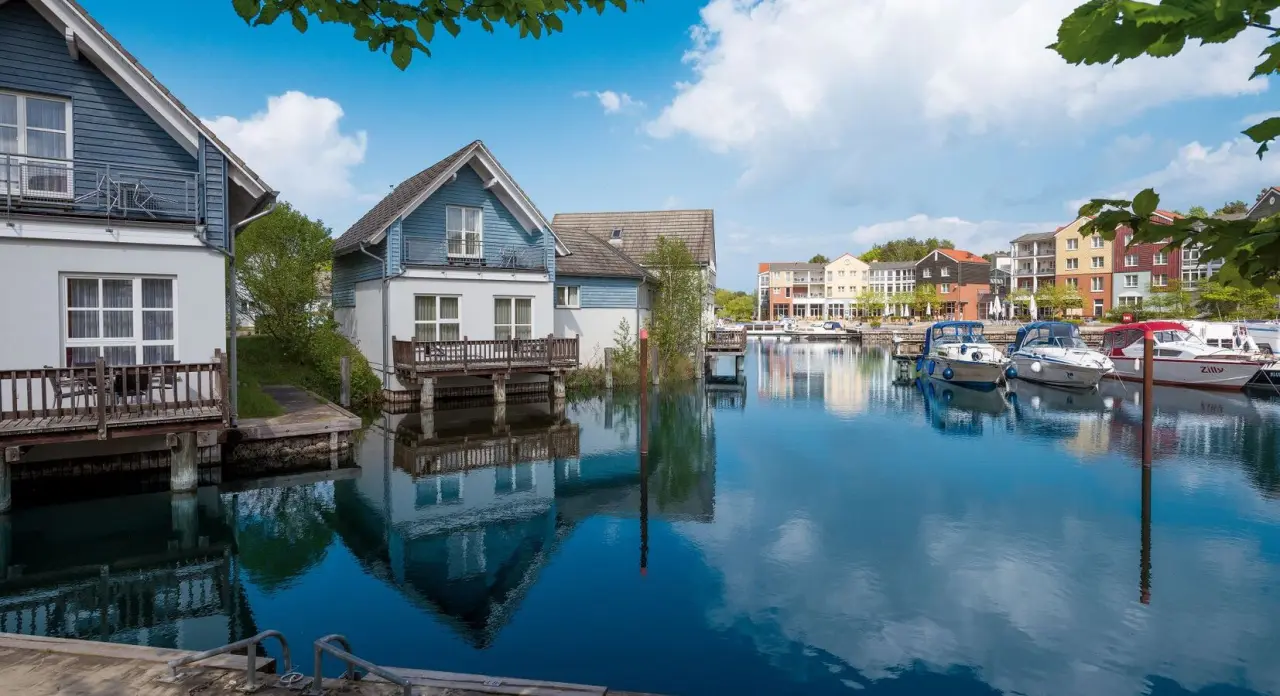 Malerische Marina des Precise Resort Marina Wolfsbruch mit bunten Häusern und Booten am Wasser unter blauem Himmel.