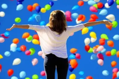 Frau mit ausgebreiteten Armen vor blauem Himmel mit bunten Ballons. Hotel Panoramic.