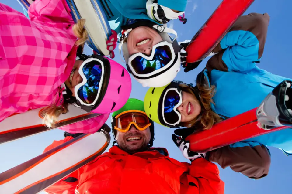 Fröhliche Skifahrer mit bunten Helmen und Skiern blicken in die Kamera, blauer Himmel im Hotel Panoramic.