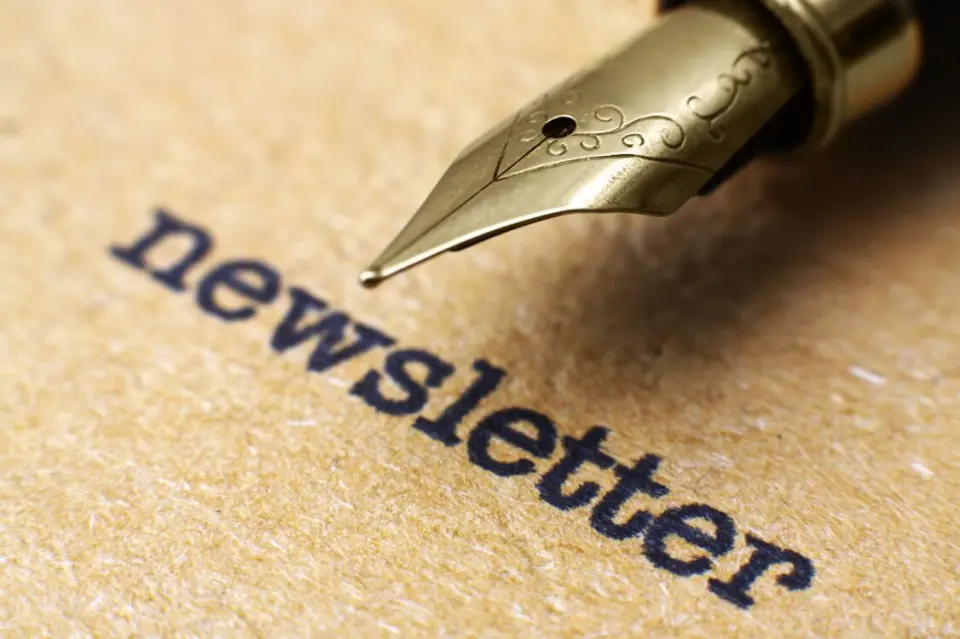 Nahaufnahme eines goldenen Füllfederhalters, der das Wort 'newsletter' auf braunem Papier schreibt.