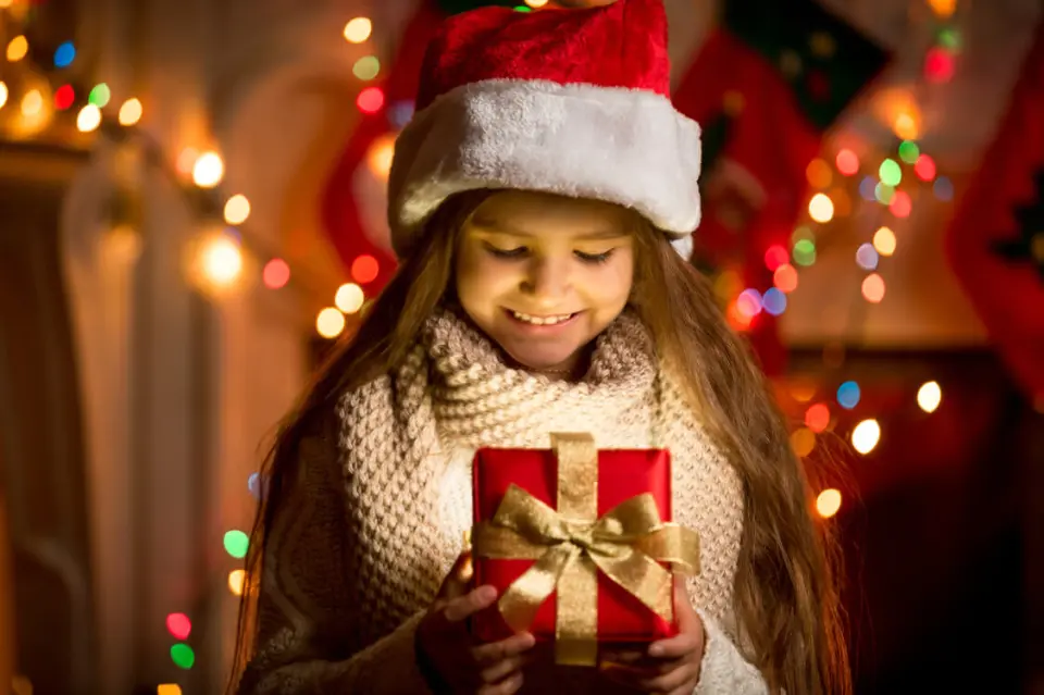 Lächelndes Mädchen mit Weihnachtsmütze und leuchtendem Geschenk vor festlicher Weihnachtsdekoration im Hotel Panoramic.