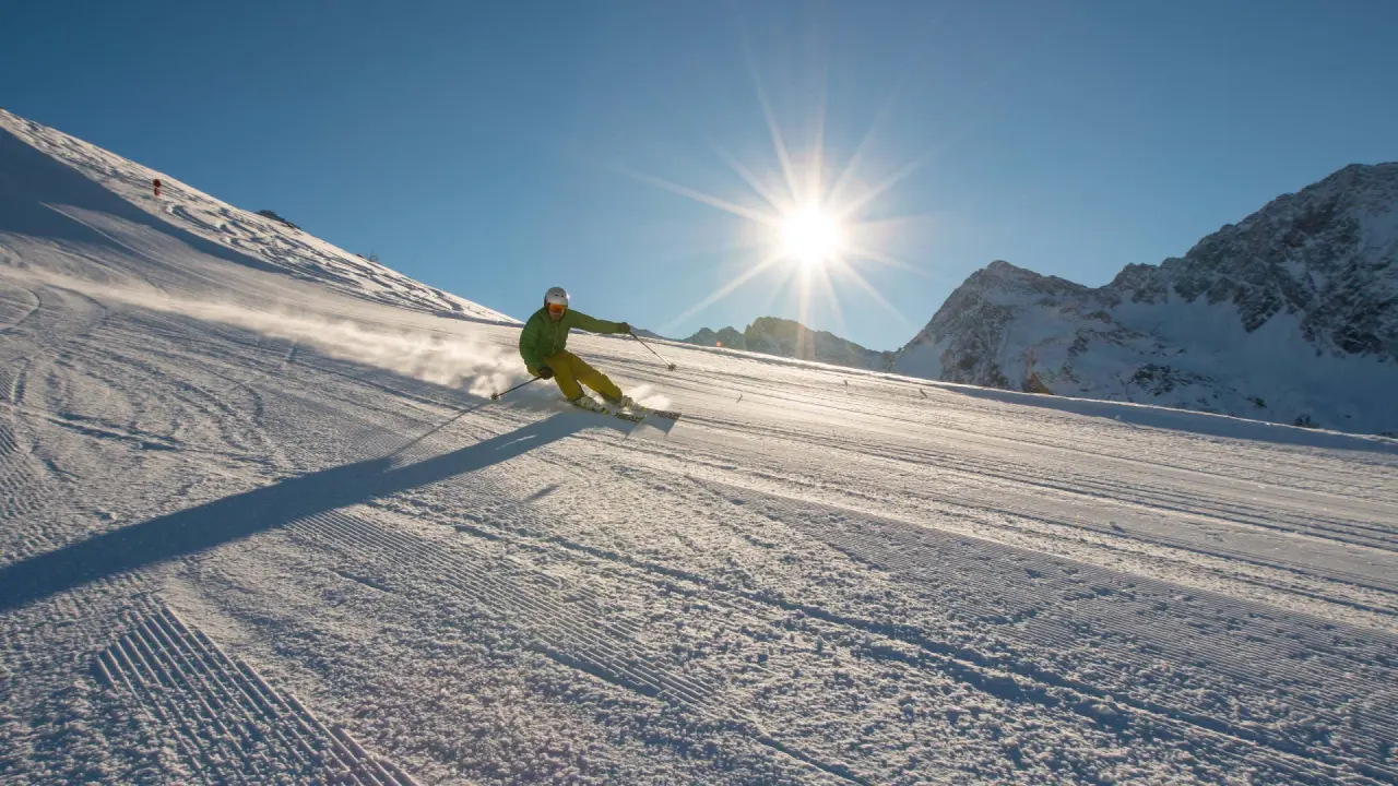 Skifahrer auf frisch präparierter Piste mit strahlendem Sonnenschein und Bergpanorama im Alpinhotel Jesacherhof.