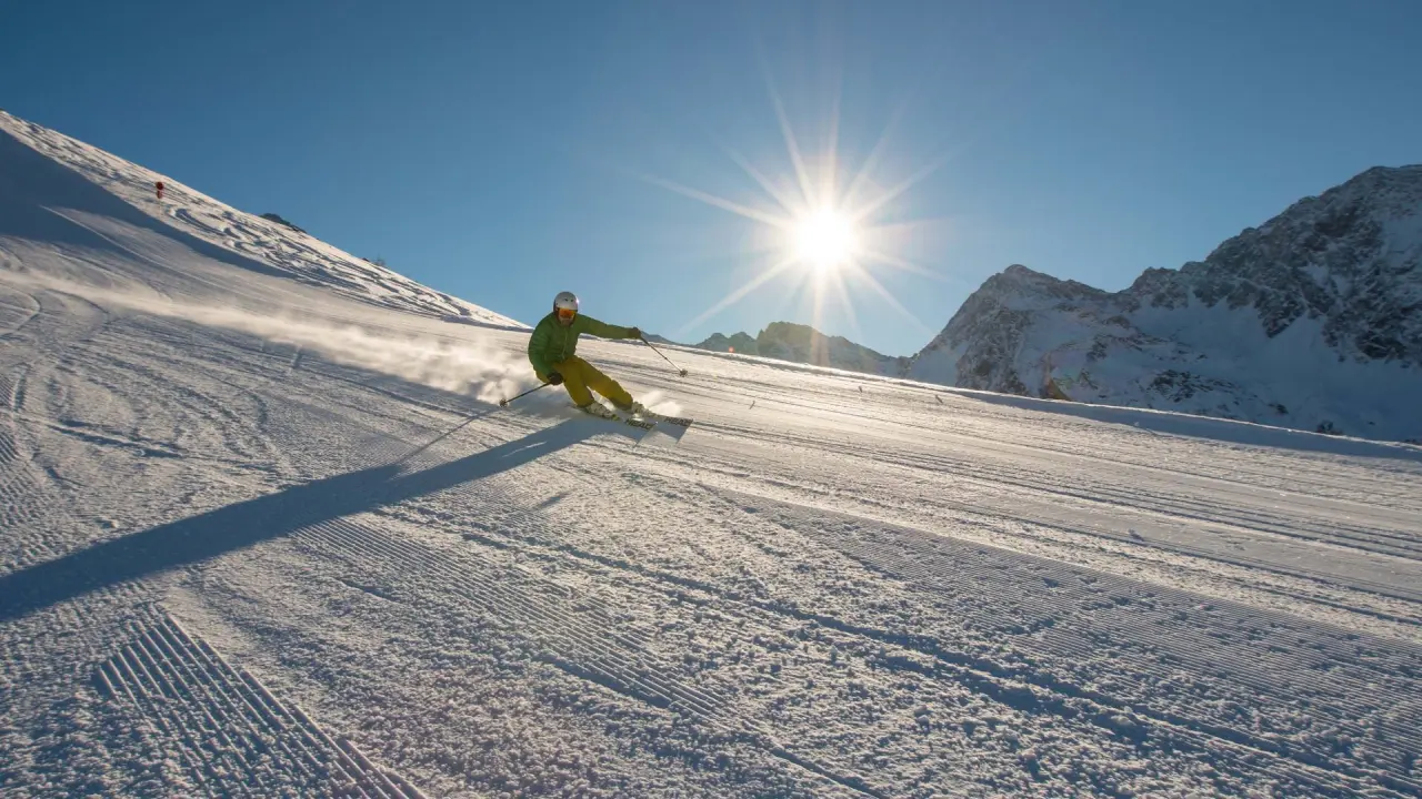 Skifahrer auf frisch präparierter Piste mit strahlendem Sonnenschein und Bergpanorama am Alpinhotel Jesacherhof.
