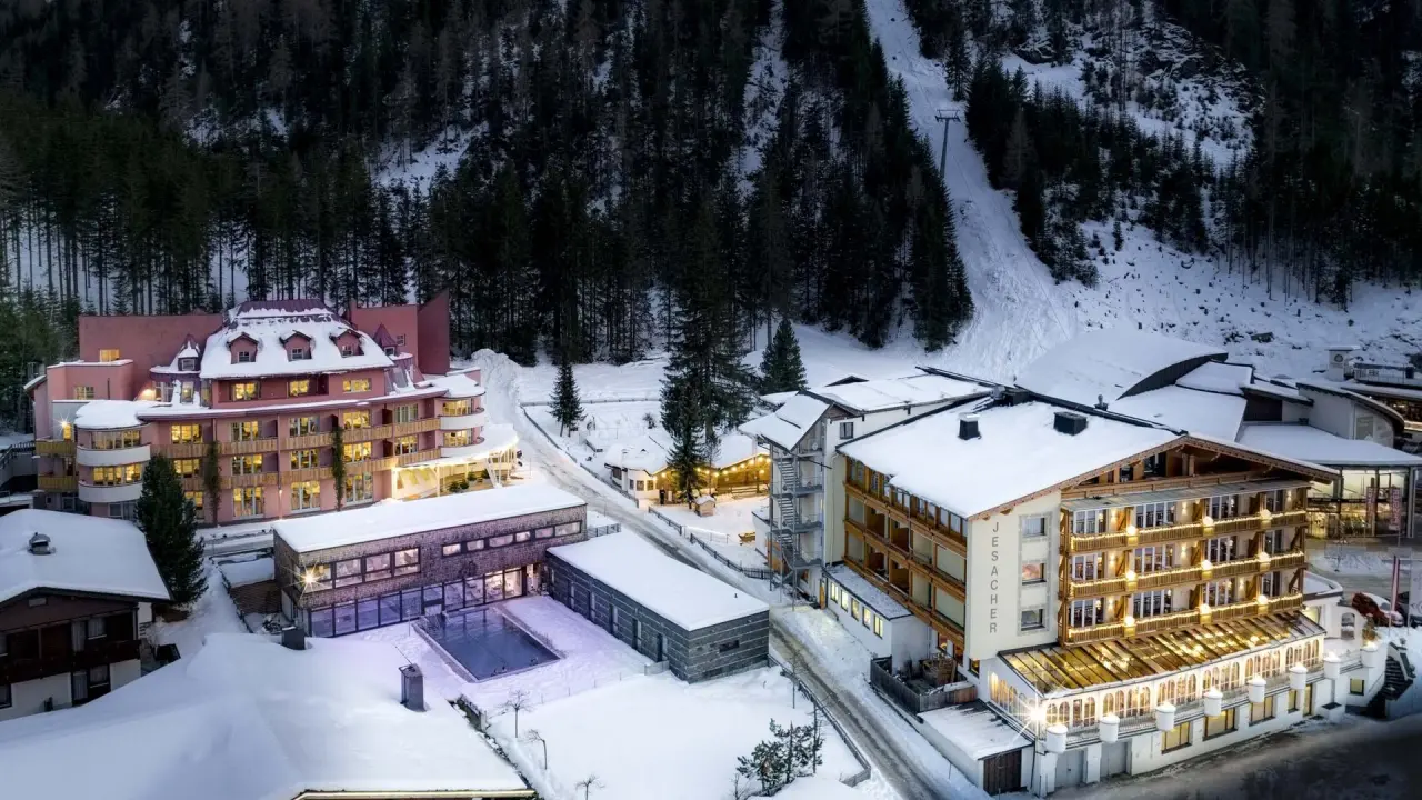 Winterliche Aussenansicht des Alpinhotel Jesacherhof mit beleuchteten Fassaden und verschneiter Berglandschaft.