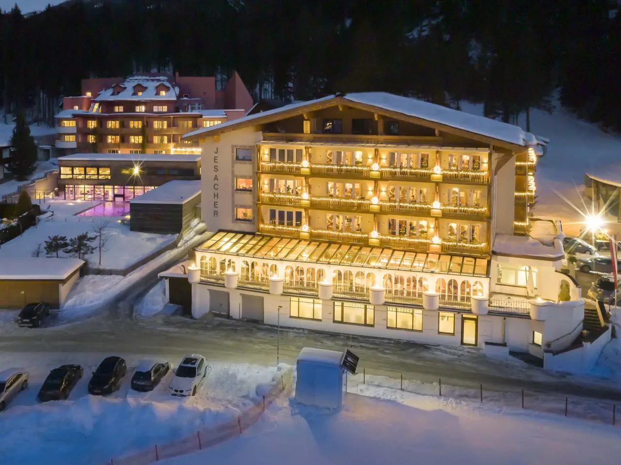 Alpinhotel Jesacherhof bei Nacht im Winter. Beleuchtetes Hotel mit Aussenpool und verschneiter Berglandschaft.