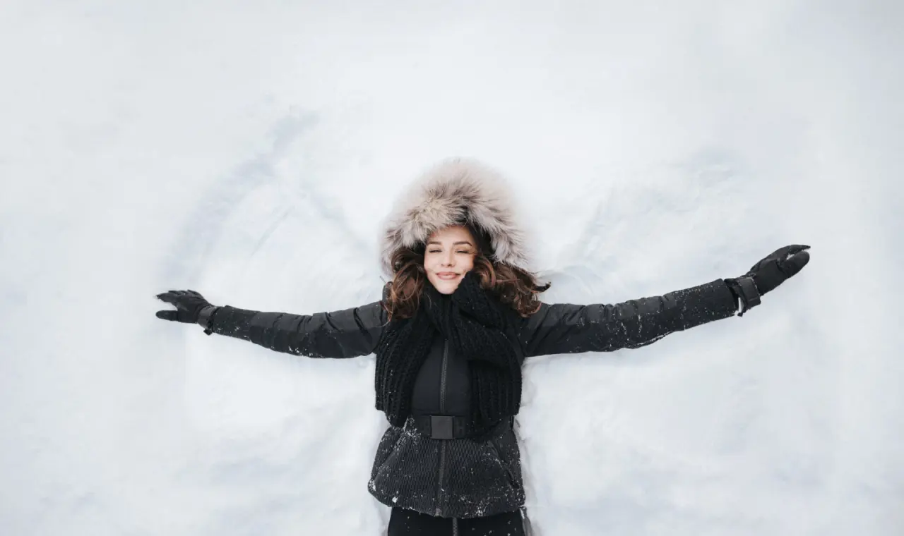 Lachende Frau macht einen Schneeengel im frischen Schnee, Wintererlebnis im Hotel Schneider.