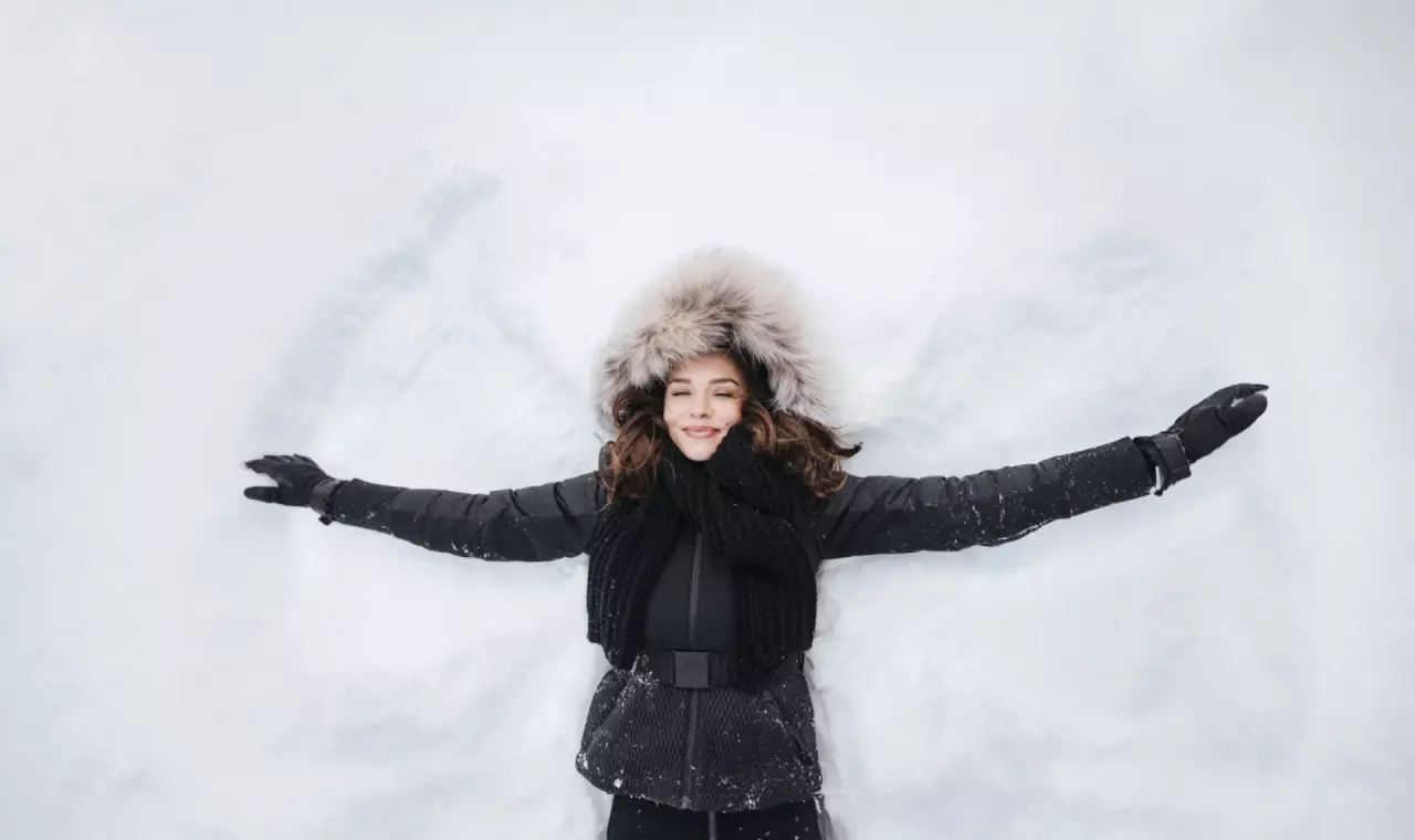Junge Frau macht einen Schneeengel im Winterurlaub im Hotel Schneider. Winterliche Entspannung und Freude im Schnee.
