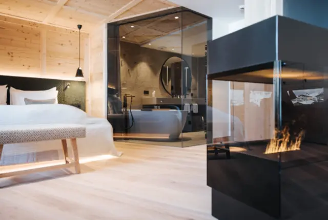 Moderne Suite im Hotel Schneider mit Holzelementen, freistehender Badewanne und Kamin für luxuriöse Entspannung.
