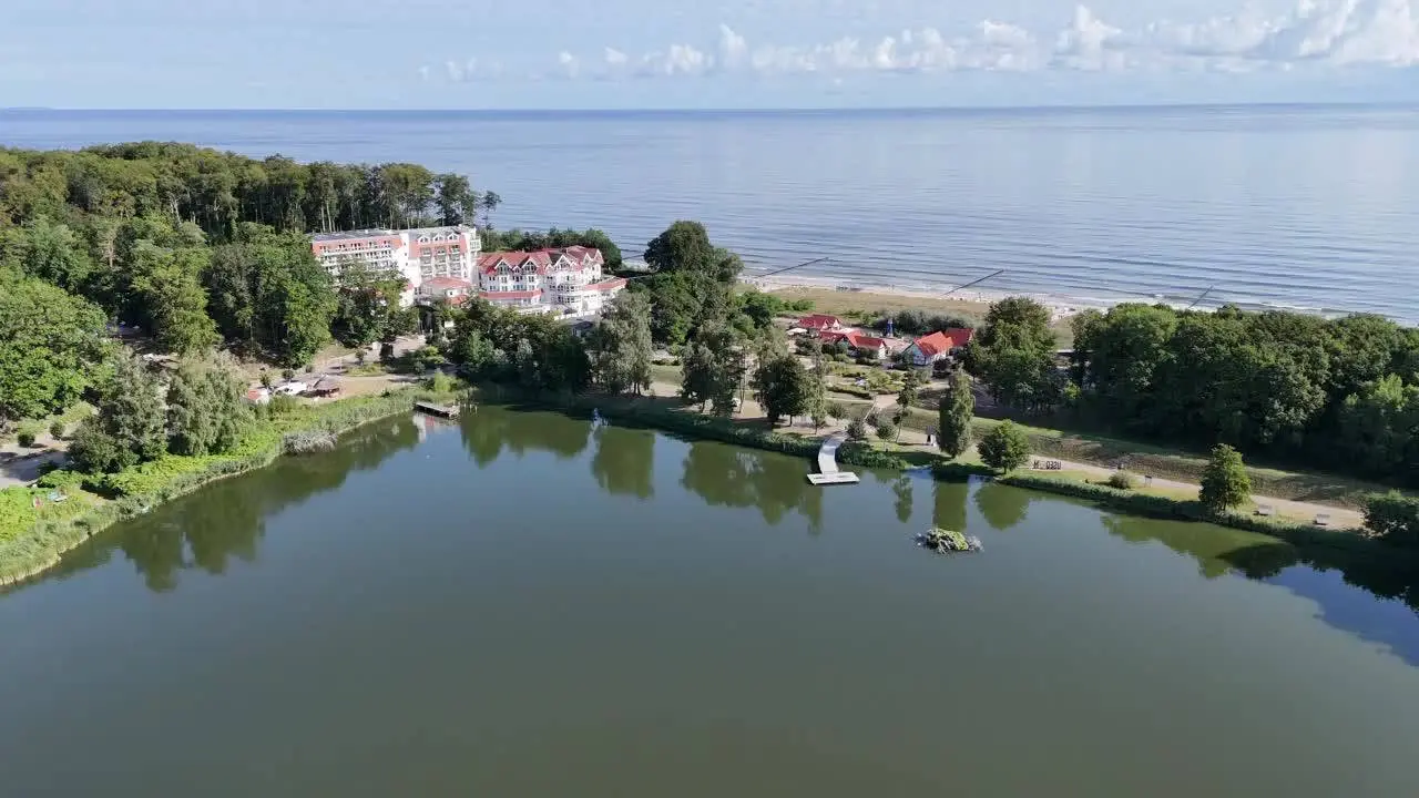 Luftaufnahme des Strandhotel Seerose an der Ostsee, idyllisch gelegen zwischen einem See und dem Sandstrand, umgeben von Wald.