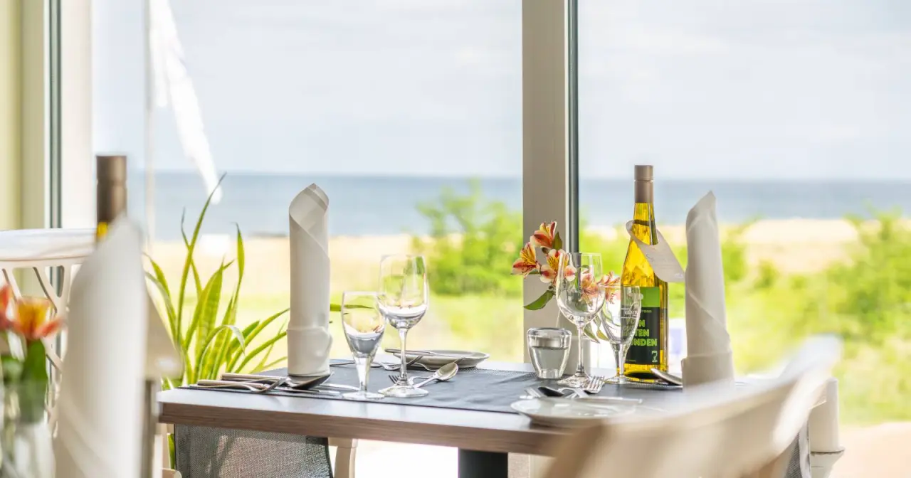 Elegant gedeckter Tisch im Restaurant des Strandhotel Seerose mit Meerblick und grüner Küstenlandschaft.